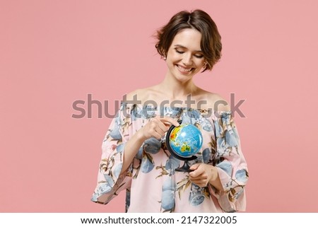 Young dreamful happy smiling geography student teacher caucasian woman with short hairdo in trendy stylish blouse spin touch Earth world globe isolated on pastel pink color background studio portrait.