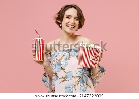 Young smiling fun caucasian woman 20s with short hairdo wearing trendy stylish blouse holding takeaway bucket with pop corn cup of soda cola isolated on pastel pink color background studio portrait.