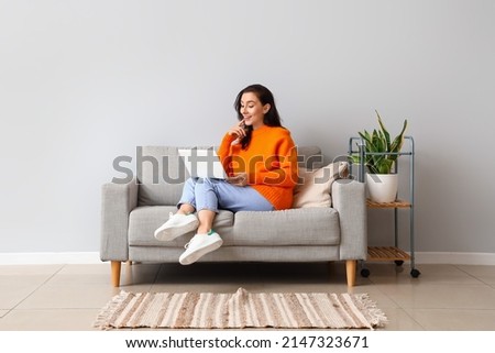 Beautiful young woman with laptop resting on couch at home Royalty-Free Stock Photo #2147323671