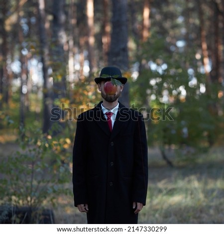 Theme of surrealism: a man in a black coat, red tie and black bowler hat with a forest in the background. Surreal depiction of a man in a suit and bowler hat, based on a painting by Rene Magritte. Royalty-Free Stock Photo #2147330299