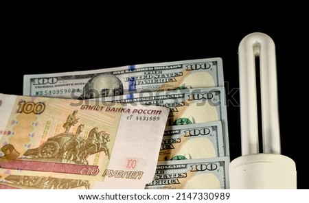 American dollars and Russian rubles, next to an economical lamp on a black background. The concept of the cost of electricity and energy