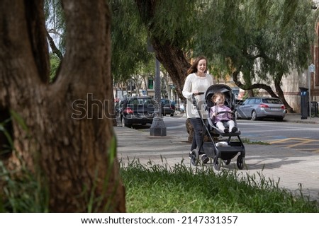 Mother walks with her little baby in a stroller in the city park Royalty-Free Stock Photo #2147331357