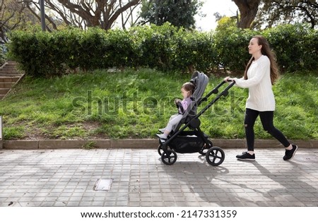 mother walks with her little baby in a stroller in the park Royalty-Free Stock Photo #2147331359