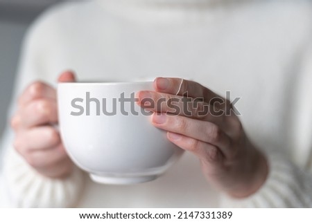 close up of woman's hands holding a big white cup of hot tea  Royalty-Free Stock Photo #2147331389