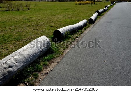 gray old logs, between lanes as protection against parking. transport solutions in the car park by the dirt road and cycle path. asphalt surfaces and lawn in the garden