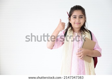cute Indian girl holding notebook for learning and thumbs up pose, education concept