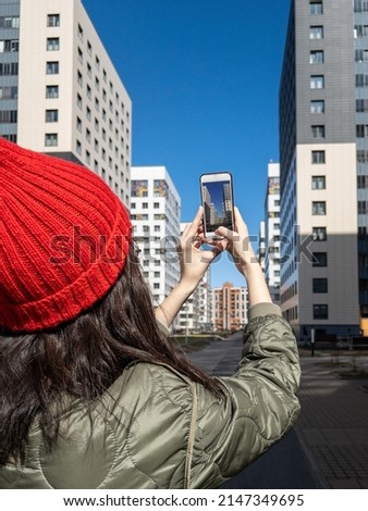 Female real estate agent in red winter hat taking a photo of property with her smartphone. Close-up of hands of realtor with the phone taking pictures of new residential buildings
