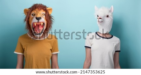 Young woman wearing lion and alpaca mask, standing and looking to the camera, isolated on blue background.