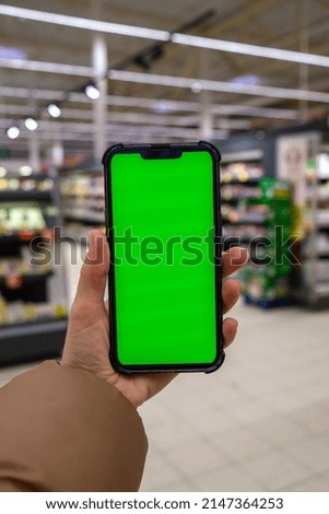 Chroma key. Close up of woman hand holds smart phone vertical with green screen at shopping mall store. Shopping center. Department store. Shopping online. Gadgets Advertisement template mock up