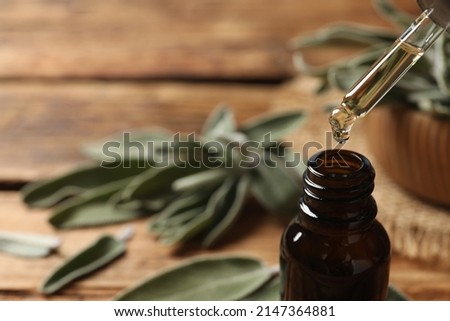 Dropping essential sage oil into bottle on blurred background, closeup. Space for text