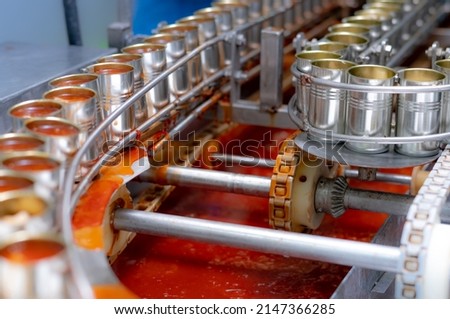 Canned fish factory. Food industry.  Sardines in red tomato sauce in tinned cans at food factory. Food processing production line. Food manufacturing industry. Many can of sardines on a conveyor belt. Royalty-Free Stock Photo #2147366285