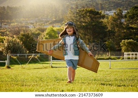 Flying on the wings of imagination. Shot of a cute little boy wearing a pilots hat and goggles while playing with cardboard wings outside. Royalty-Free Stock Photo #2147373609