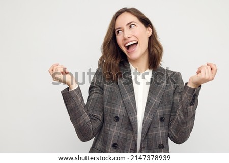 Portrait of beautiful young businesswoman looking happy to the left with arms in the air. Big smile on her face, looking beautiful and cheerful standing isolated on white background.