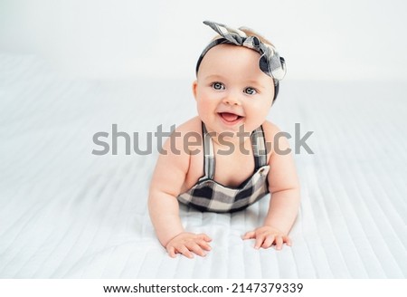 Seven month old baby child sitting on bed. Cute smiling little infant girl on white soft blanket. girl wearing headband. Charming blue eyed baby. Copy space. Royalty-Free Stock Photo #2147379339