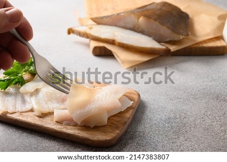 Smoked halibut slices on gray background. Man eating delicacy fish. Close up.