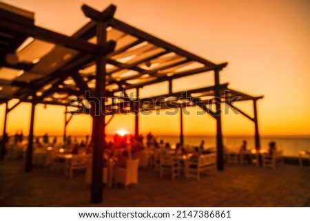 Abstract blurred image of outdoor restaurant terrace on warm summer evening sunset over the sea with bokeh for background. Holiday, vacation and travel concept