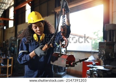 Technician engineer or worker woman in protective uniform with safety hardhat standing and maintenance operation or checking overhead crane remote control at heavy industry manufacturing factory Royalty-Free Stock Photo #2147391203