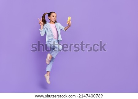 Photo of cute shiny little school girl wear denim shirt jumping tacking selfie device v-sign empty space isolated purple color background