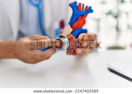 Young caucasian man wearing doctor uniform auscultating heart at clinic
