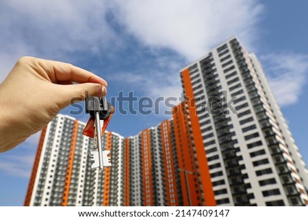 House keys in male hand on background of new buildings. Real estate agent, moving home or renting property