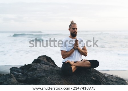 Caucasian man in casual wear have holistic therapy practice for feeling vitality during weekend morning at seashore, young male in namaste asana praying mantras reaching appeasement and mindfulness Royalty-Free Stock Photo #2147418975