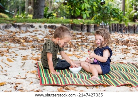 Two small children on a picnic eating strawberries together. Siblings eat berries and laugh. Happy children. Healthy nutrition of young children.