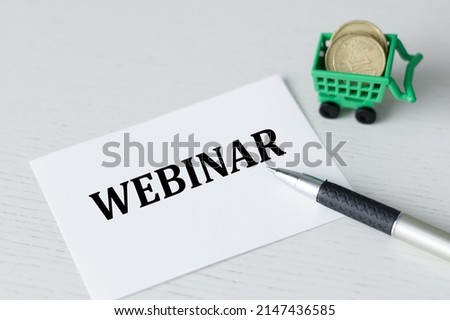 a white card with webinar text on a bright table next to a pen and coins in a basket, business concept