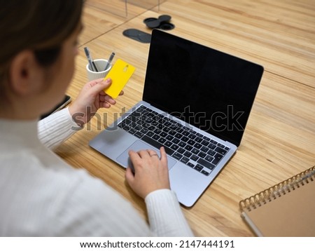 rear view of a woman with a credit card in front of a laptop