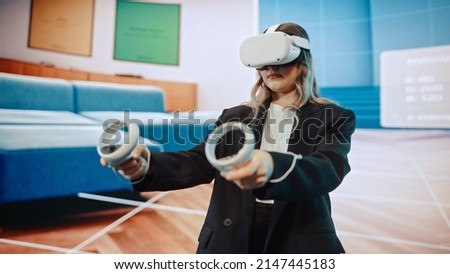 Interior Designer Using a VR Software to Design a Living Space. Change Couch Colors, Move Furniture in Interactive Environment on a Big Digital Screen. Female Engineer Using Headset and Controllers.