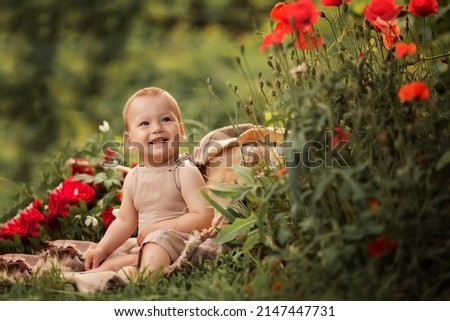 Baby boy sits in the garden on the grass laughs and looks away. Near red flowers