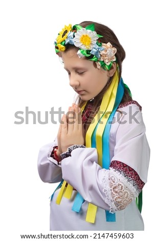 A little girl in national Ukrainian clothes with tearful eyes folded her hands in front of her and prays for an end to the war in Ukraine. Studio photo on a white background.