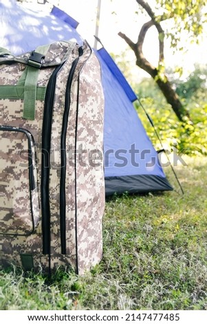 Defocus blue open tourist tent standing on green nature background. Army backpack. Tourism concept. Summer vacation in forest, camping. Wild nature. Hiking. Closeup. Vertical. Out of focus.