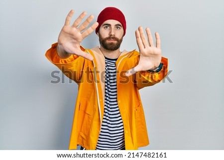Caucasian man with beard wearing yellow raincoat doing frame using hands palms and fingers, camera perspective 