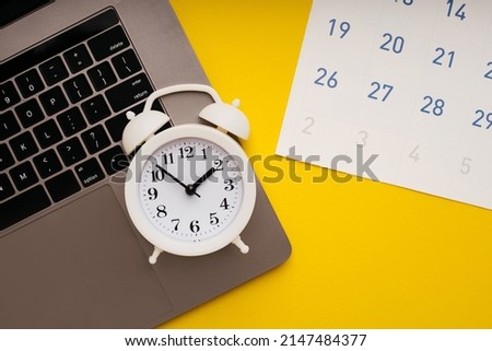 Laptop, monthly calendar and alarm clock on yellow background. Deadline concept.