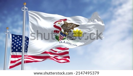 The Illinois state flag waving along with the national flag of the United States of America. In the background there is a clear sky. Illinois is a state in the Midwestern region of the United States Royalty-Free Stock Photo #2147495379