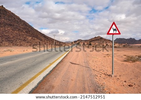 Empty desert road at Wadi Rum, red triangle warning camels sign near