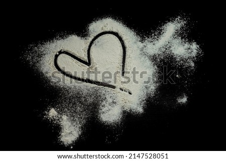 Black background sprinkled with flour heart shape, smeared flour, table for cooking, rolling dough. Preparing for baking, top view isolated on a black background or table. Love concept.