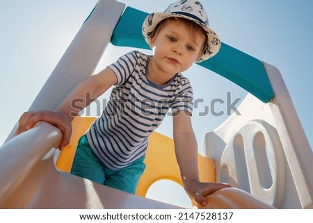 A portrait of a little boy with a striped shirt on top of a slider with a blue sky background behind him