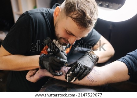 Tattoo master is tattooing a man's hand. Wireless tattoo machine, safety and hygiene at work. Close-up of tattoo artist work. Tattoo salon Royalty-Free Stock Photo #2147529077