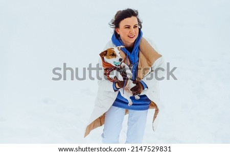 Happy woman with a smile on her face and with a small dog breed Jack Russell in her arms having fun on the street in the snowfall in the snow.