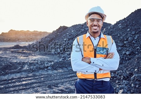 A young African mine worker wearing protective wear is looking at the camera with coal mine in the background Royalty-Free Stock Photo #2147533083