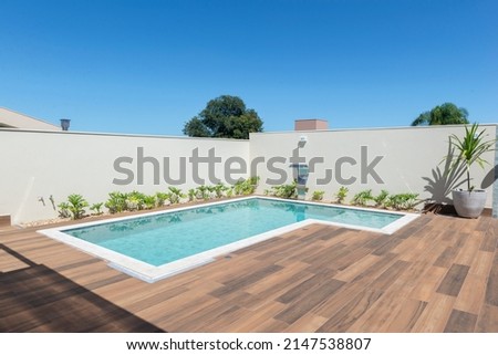 "L" shaped pool design in modern residence. Swimming pool with solar heating, clear and bluish on a sunny day. Ceramic floor with wood texture. Swimming pool with artificial metal waterfall.