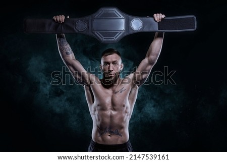 Kickboxer victoriously raises the belt won in the tournament against the backdrop of smoke. Sports competitions. Fight night. The concept of mixed martial arts. MMA Royalty-Free Stock Photo #2147539161