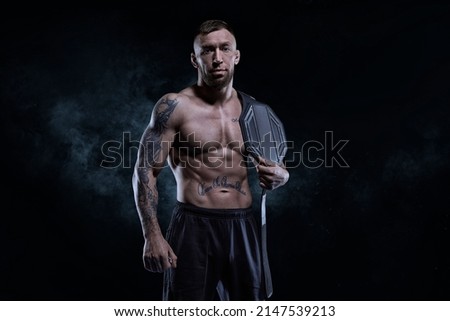 Kickboxer with a belt on his shoulder poses against a background of smoke. Sports competitions. Fight night. The concept of mixed martial arts. MMA