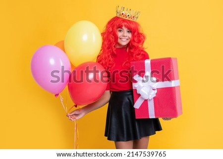 happy girl in crown with present box and party balloon on yellow background