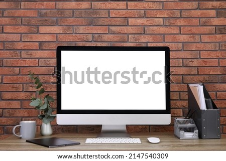 Modern computer with blank screen on desk near brick wall, space for design. Comfortable workplace