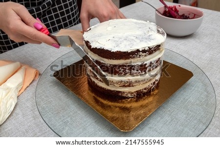 Women's hands with the help of kitchen spatula touch sponge cake. Close-up. Selective focus. Picture for articles about food, cooking, confectioners.