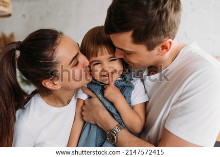 Portrait of a happy young family. Happy family mother, father, little daughter. A happy young family spends time together in a home interior. Mom and dad kiss their baby. Happy child with parents
