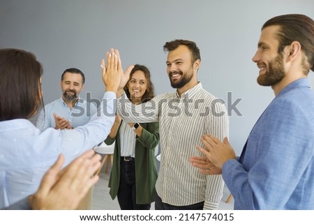 Woman gives five to her happy successful male colleague to applause of other business people. Colleagues support each other at company's seminar. Concept of business, respect, cohesion and teamwork. Royalty-Free Stock Photo #2147574015