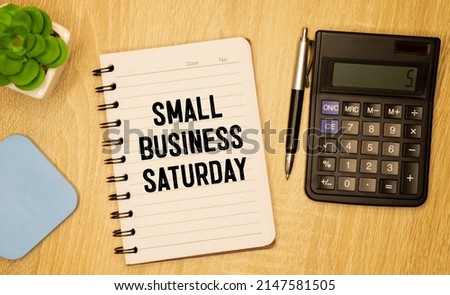 Text Small Business Saturday in notebook on white table with office tools